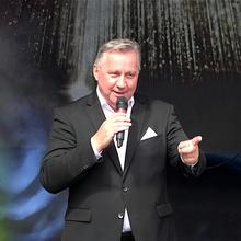Ein Mann steht auf einer Bühne, hat in der rechten Hand ein Mikro und zeigt mit der linken Hand nach vorn. ©California Promotion